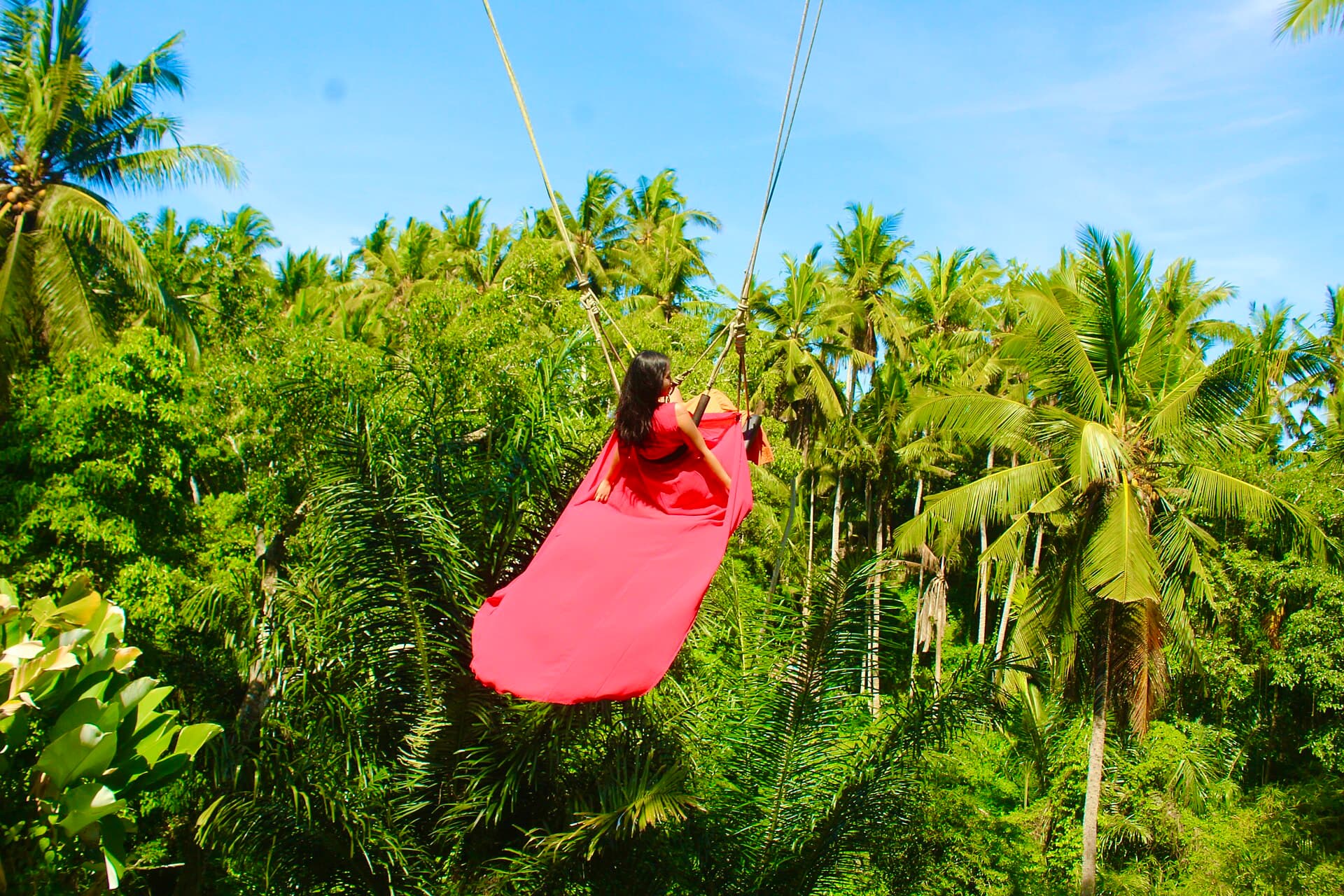Vrouw in rode jurk op een reuzenschommel boven de jungle bij Ubud